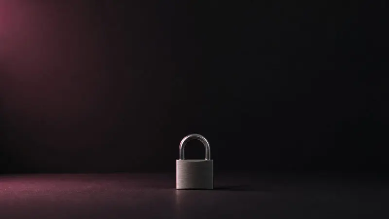 A small brushed-steel padlock on a dark matte surface, lit by a soft rose glow