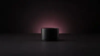 A plain black leather cuff standing on a dark surface, backlit by a soft rose glow