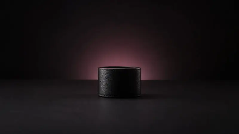 A plain black leather cuff standing on a dark surface, backlit by a soft rose glow