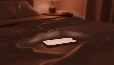 A phone glowing on satin sheets casting rose-gold light