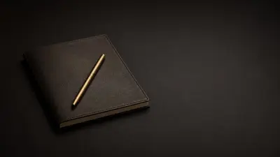 A closed leather notebook with a brass pen resting on it, on a dark matte surface