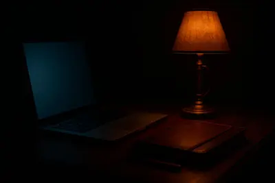 A dimly lit desk with a laptop and notebook